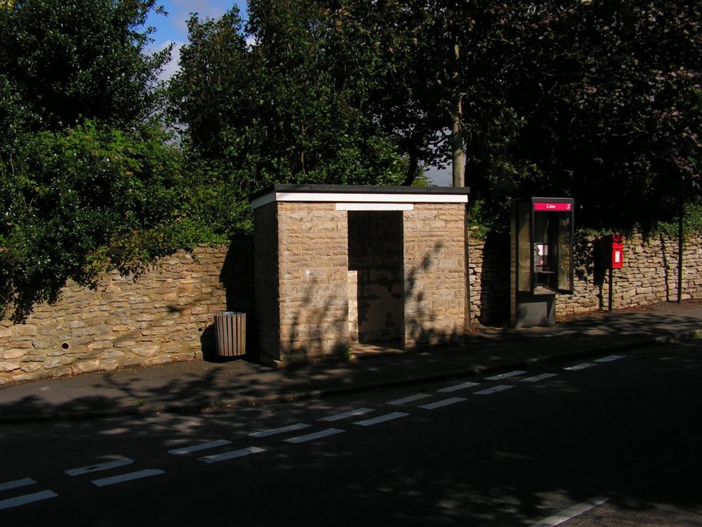 A stone bus shelter beside a stone wall, with a telephone box and a red post box