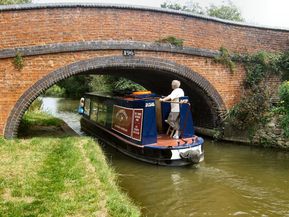 A narrowboat passing under the red-brick humpbacked canal bridge numbered 196