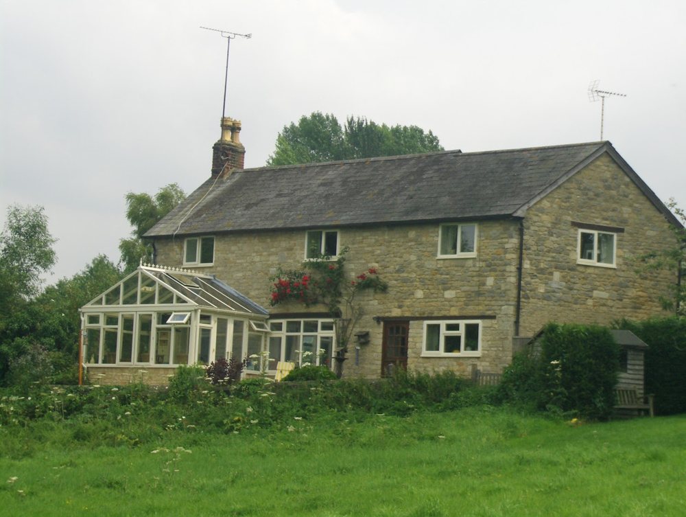 The Coach House, a two-storey stone house with a slate roof and a conservatory, seen across the field